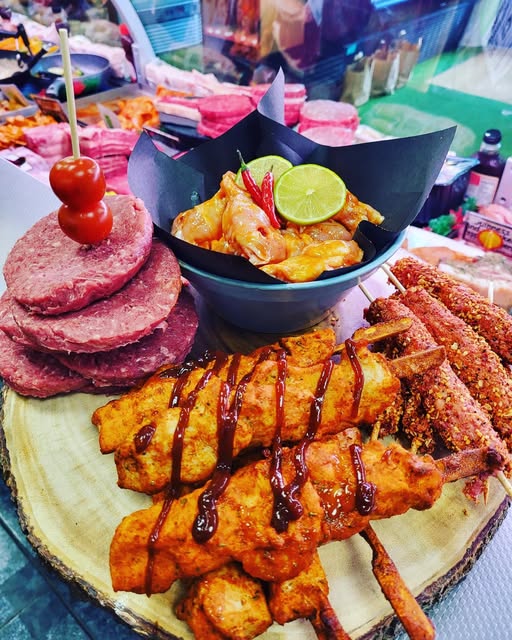 Handmade burgers, marinated chicken and kebabs on the counter at The Saucy Butcher, with the meat display behind